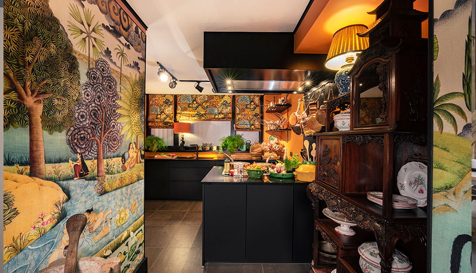 Cuisine aux meubles noirs, décorée de fresques murales colorées et d'étagères en bois avec vaisselle blanche et cuivre.