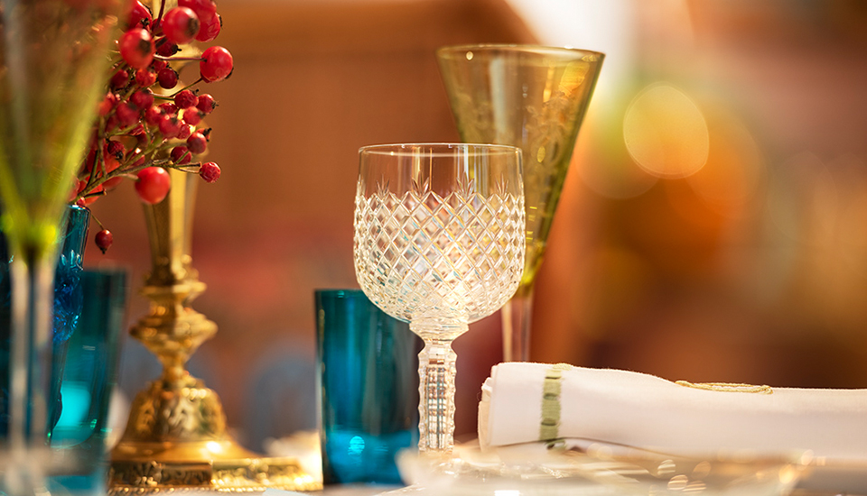 Un verre en cristal transparent est entouré de verres colorés et de baies rouges sur une table décorée avec une serviette blanche.