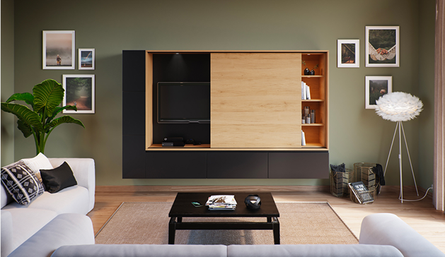 Meuble mural noir et bois avec télévision et étagères, entouré de cadres photo, dans un salon moderne avec canapé blanc et plante verte.