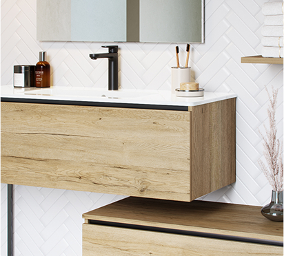 Un meuble en bois clair avec un lavabo blanc et un robinet noir est placé devant un mur carrelé en chevrons blancs.