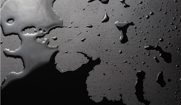Des gouttes d'eau sont dispersées sur une surface noire lisse, formant des motifs irréguliers avec des reflets lumineux.