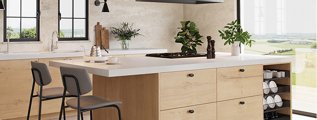 Cuisine moderne avec îlot central en bois clair, chaises grises, plantes vertes et vaisselle blanche, éclairée par une grande fenêtre.