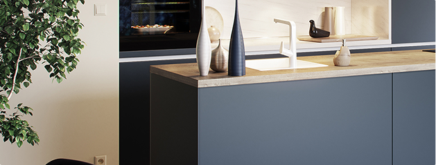 Cuisine moderne avec des armoires bleues, un plan de travail en bois clair, des vases décoratifs, et un four encastré au fond.