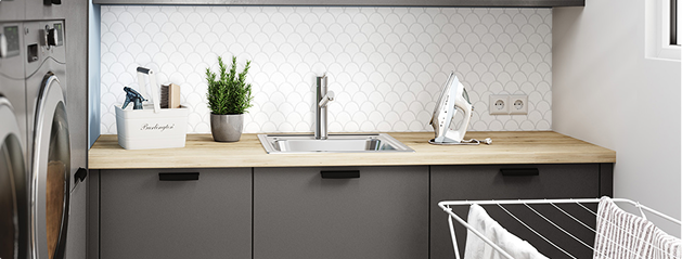 Cuisine moderne avec plan de travail en bois clair, évier en inox, plante en pot, fer à repasser blanc et étendoir à linge.