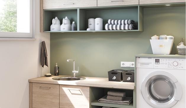 Une buanderie moderne avec un évier en acier inoxydable, des étagères vertes, des bouteilles blanches, des serviettes pliées et une machine à laver blanche.