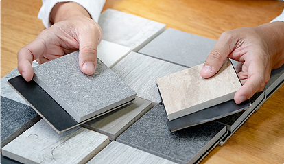 Des mains tiennent des échantillons de carrelage de différentes textures et couleurs sur une table en bois.