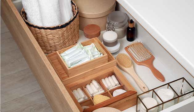 Produits de toilette organisés dans un tiroir avec des boîtes en bambou, une brosse à cheveux en bois, des serviettes blanches et divers contenants.