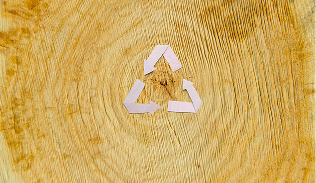 Icône de recyclage en papier blanc posée sur une surface en bois avec des cernes visibles.
