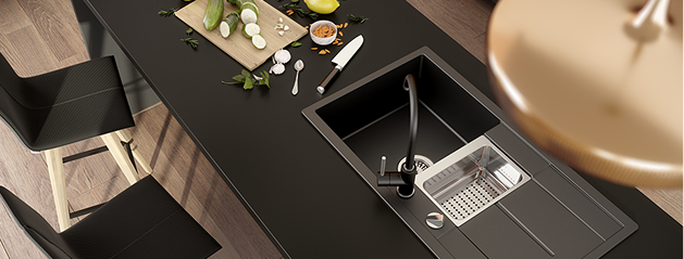Plan de travail de cuisine noir avec évier intégré, planche à découper avec légumes, couteau et cuillères disposés sur la surface.
