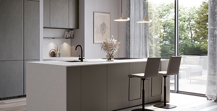 Cuisine moderne avec îlot central gris, deux tabourets, luminaires suspendus et grandes fenêtres donnant sur un jardin verdoyant.