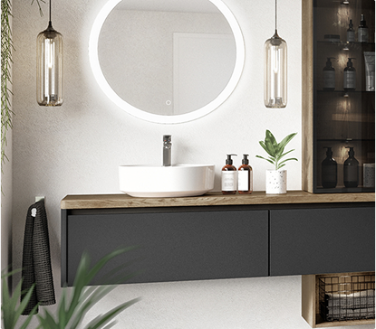 Meuble de salle de bain avec vasque blanche, miroir rond éclairé, plantes vertes, et étagères ouvertes contenant des accessoires.