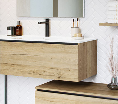 Meuble de salle de bain en bois clair avec lavabo blanc, robinet noir, et accessoires sur fond de carrelage blanc en chevrons.