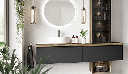 Une salle de bain moderne avec un meuble noir, un lavabo blanc, un miroir rond éclairé, des flacons, une plante verte et des lampes suspendues.