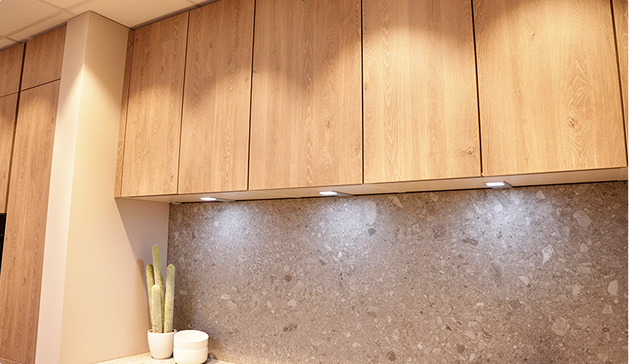 Placards en bois clair au-dessus d'un plan de travail en pierre grise, avec deux pots blancs contenant des plantes vertes.