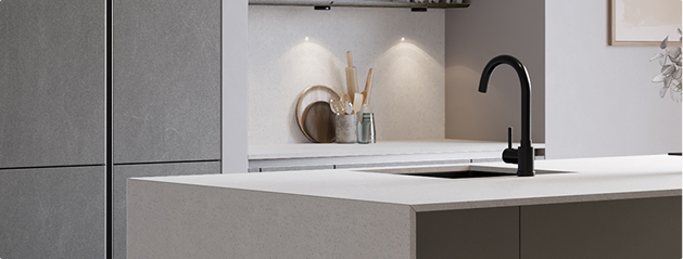 Cuisine moderne avec un îlot central en pierre grise, évier noir, planche à découper et ustensiles en bois sous éclairage intégré.