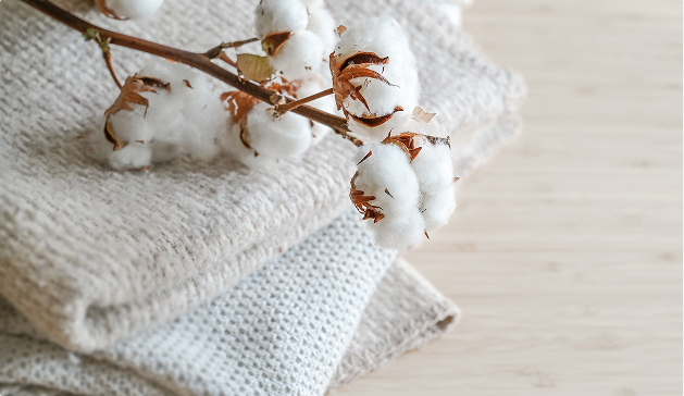 Branche de coton blanche posée sur des serviettes en tissu beige et gris, disposées sur une surface en bois clair.