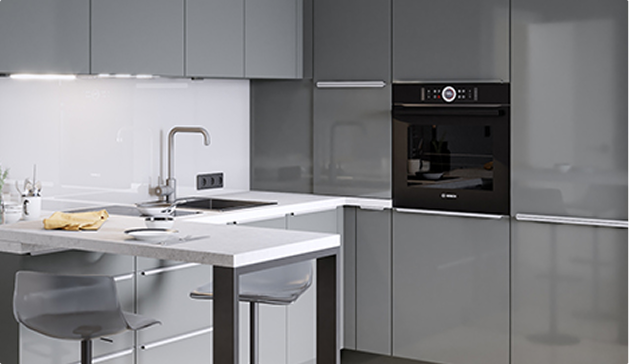 Cuisine moderne avec armoires grises, plan de travail blanc, four encastré noir et tabouret transparent près de l'îlot central.