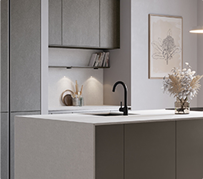 Cuisine moderne avec un îlot central gris, évier noir, étagères intégrées, décoration murale et vase de fleurs séchées sur le plan de travail.