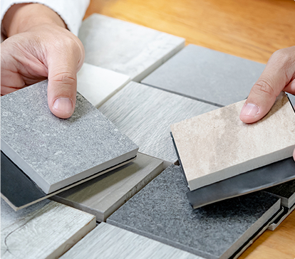 Des mains tiennent et comparent des échantillons de carreaux de différentes textures et couleurs, disposés sur une table en bois.
