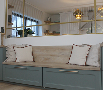 Banquette en bois clair avec coussins beiges et bordures marron, située devant une cloison vitrée dorée, dans un intérieur moderne.