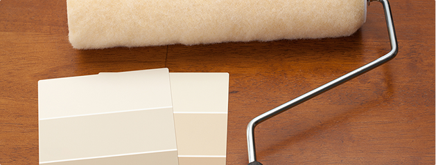 Un rouleau à peinture beige et des échantillons de couleurs sont posés sur une table en bois brun.