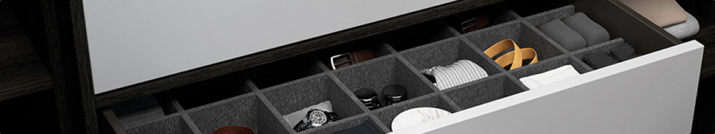 Tiroir ouvert avec des compartiments contenant des ceintures, une montre, des vêtements pliés et des accessoires divers.